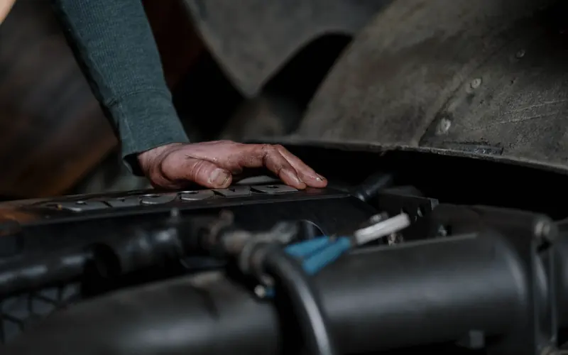 A hand resting on an engine cover under a raised bonnet