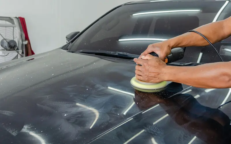 Hands holding a machine polisher on the bonnet of a dark car