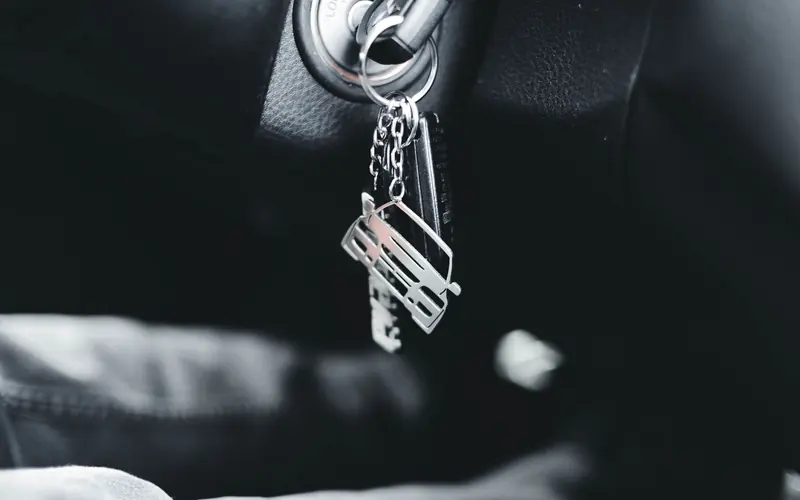 A set of car keys hanging from a car's ignition, with a car-shaped keyring